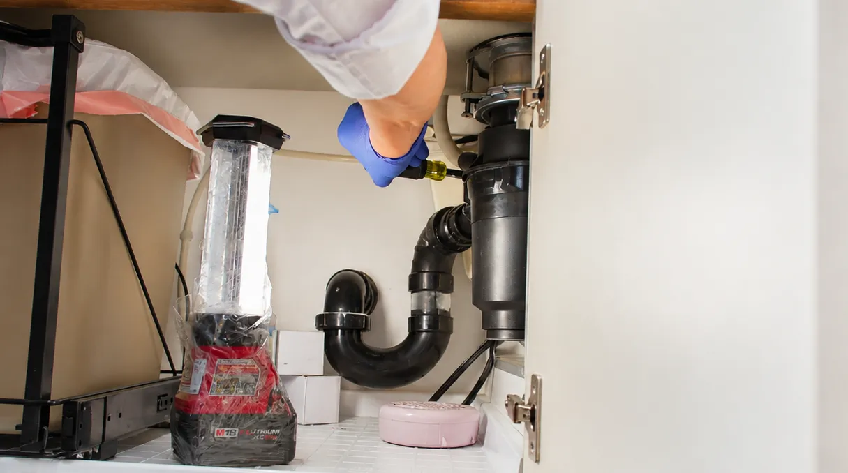 Plumber tightening a garbage disposal under a kitchen sink