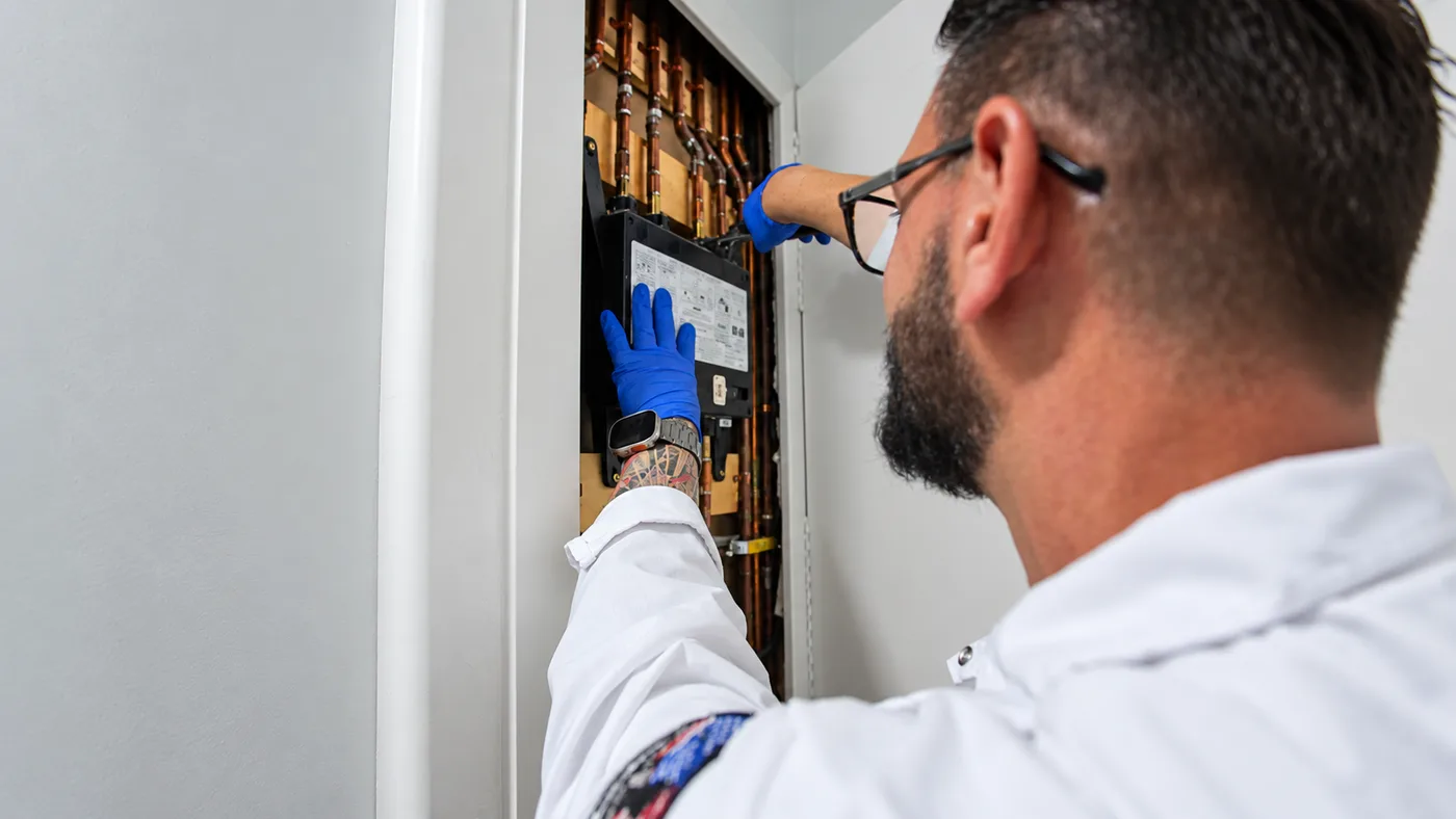 Plumber inspecting copper water lines behind an access panel